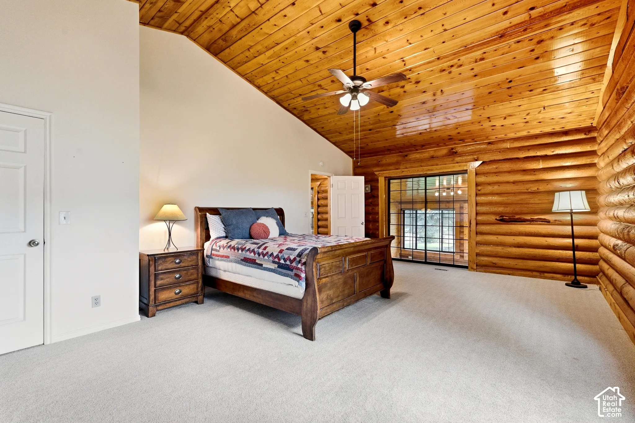 Vaulted wood-paneled ceiling with a ceiling fan, log walls, and light-colored carpeting