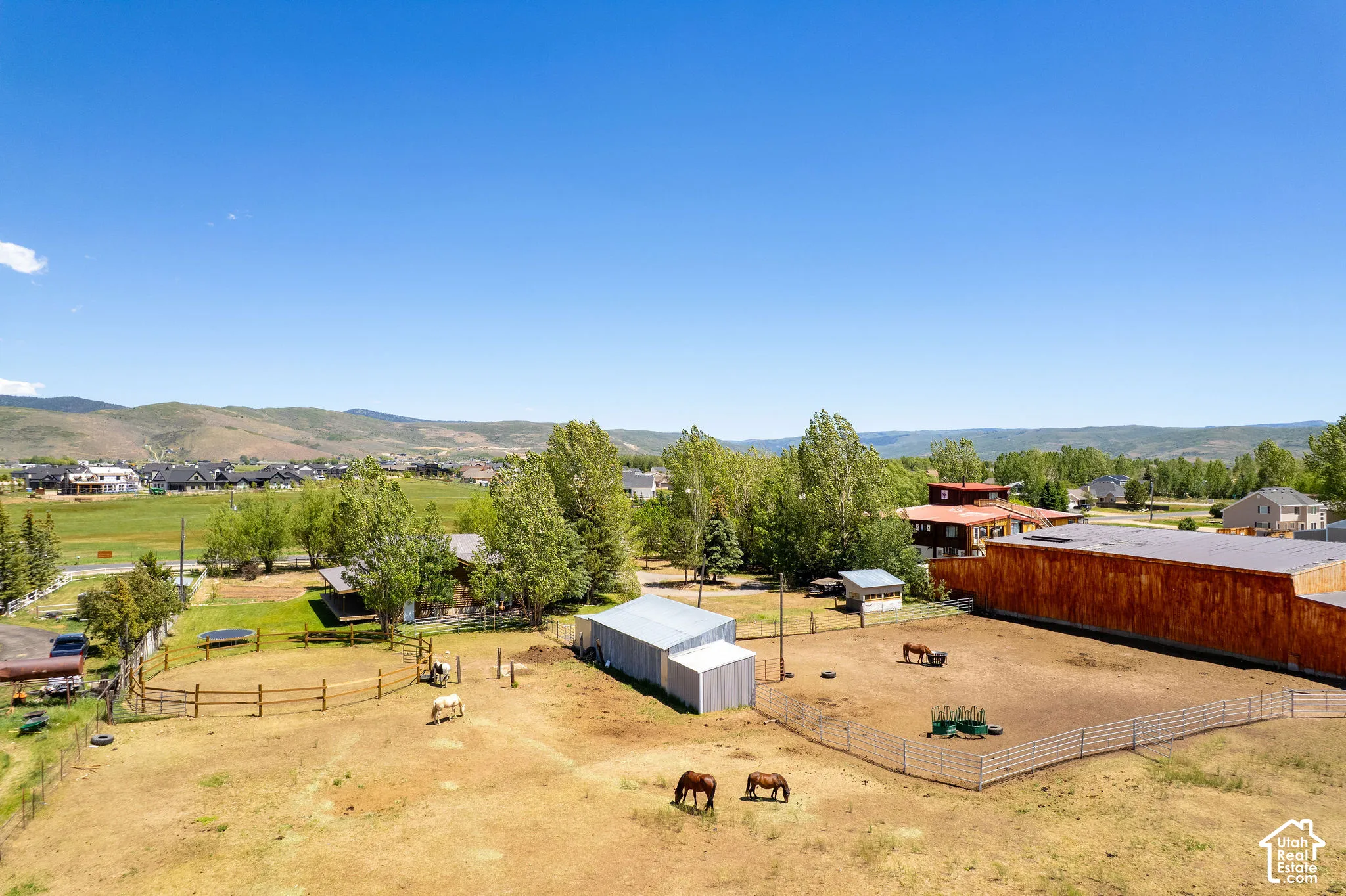 Expansive property with multiple fenced pasture areas, an enclosed barn structure, a large outbuilding, and distant mountain scenery