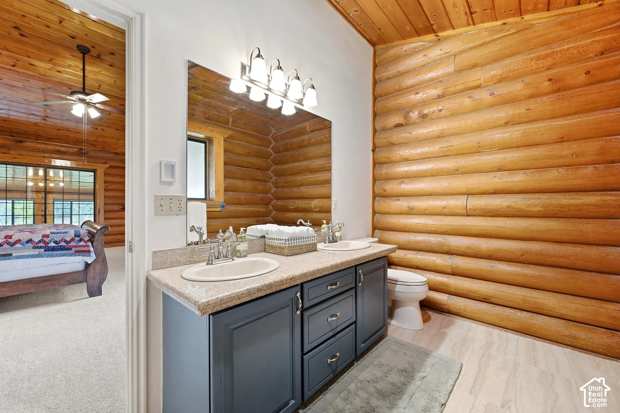 Dual sink vanity with dark cabinetry, light countertop, and wall-mounted lighting