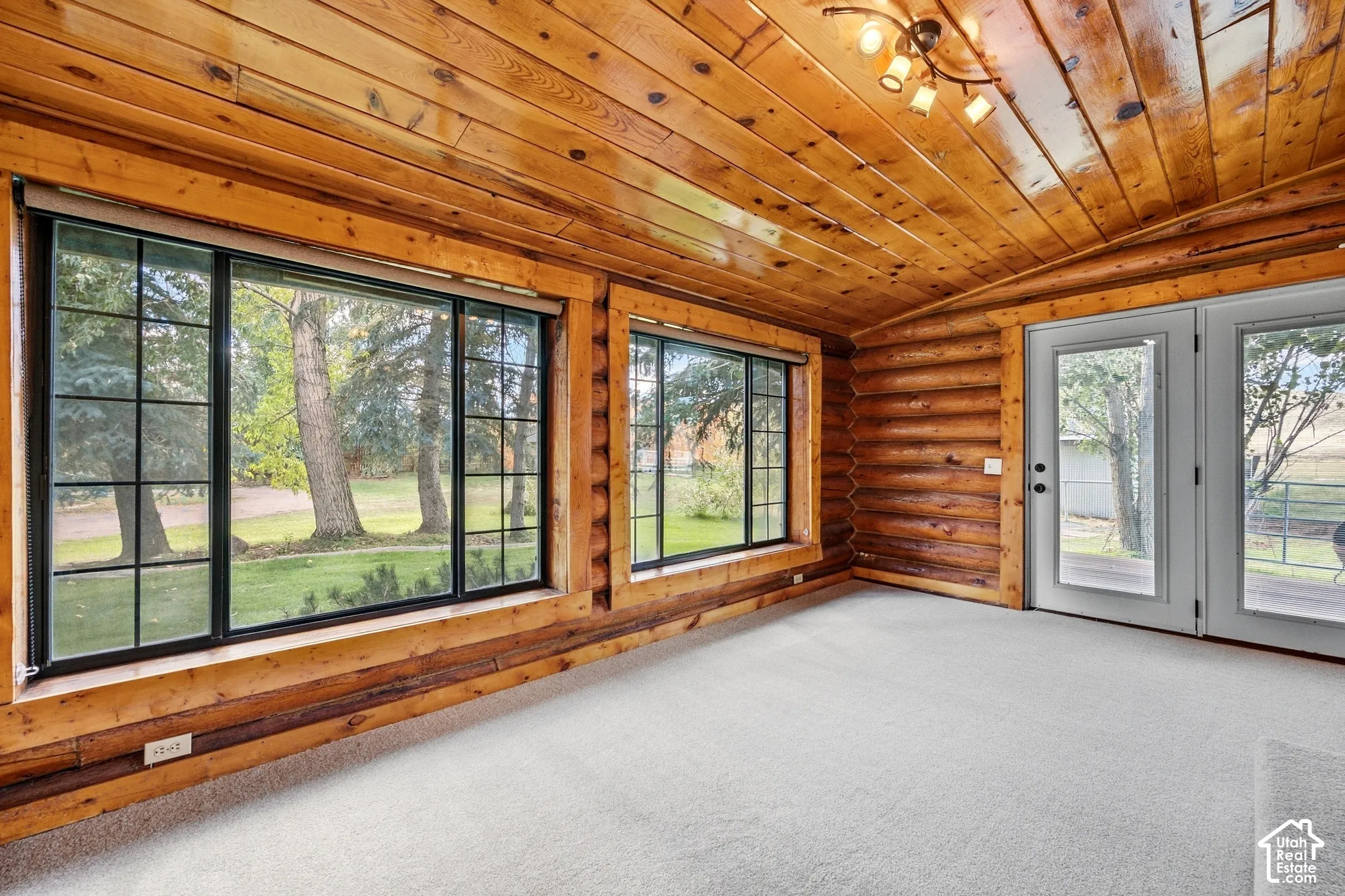 Wood-paneled ceilings, wood-log walls, light-toned carpeting, black-framed windows, and white-framed glass doors