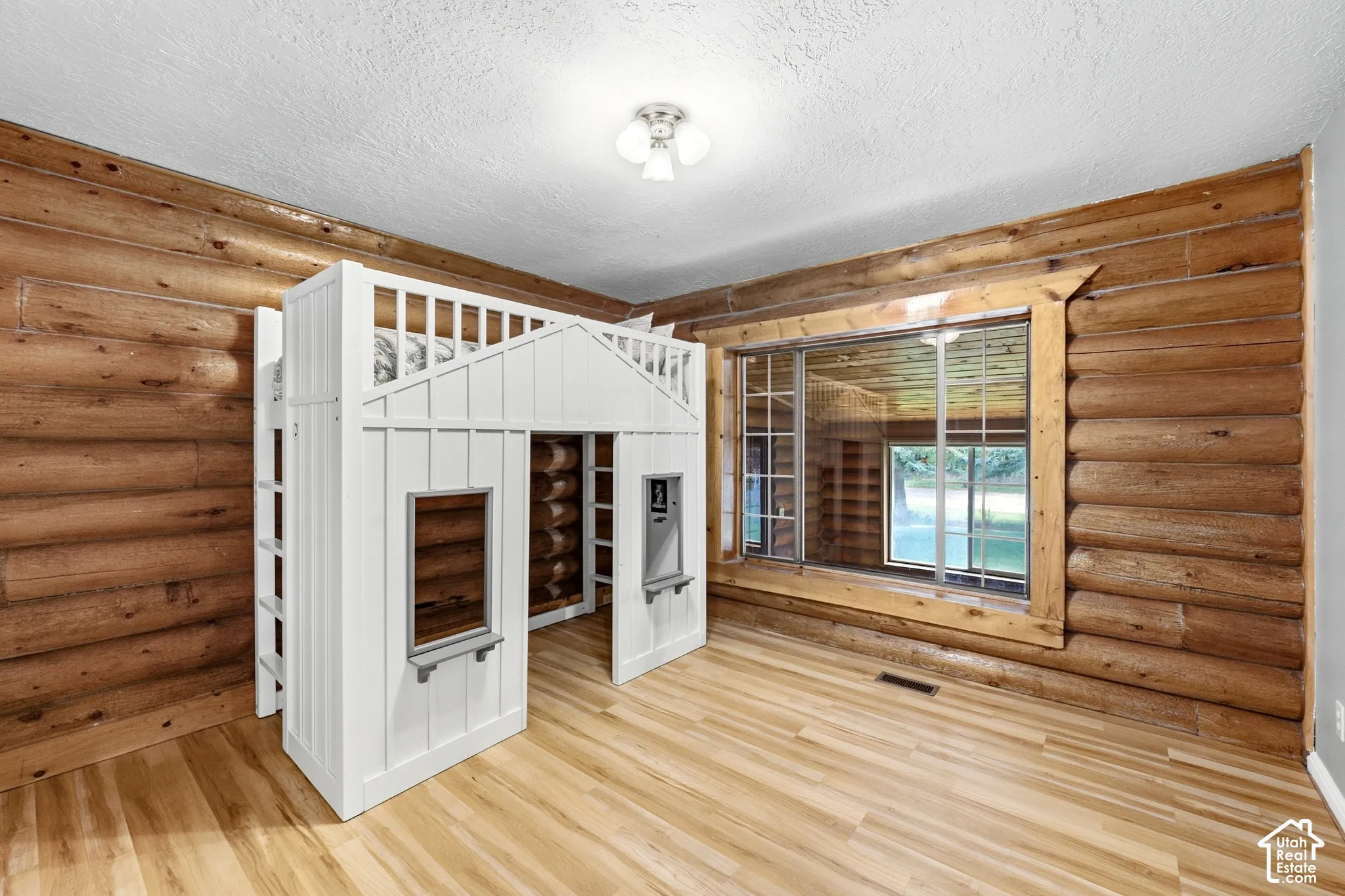 Log wall construction, wood-finish flooring, built-in loft bed with integrated playhouse, and a multi-pane window