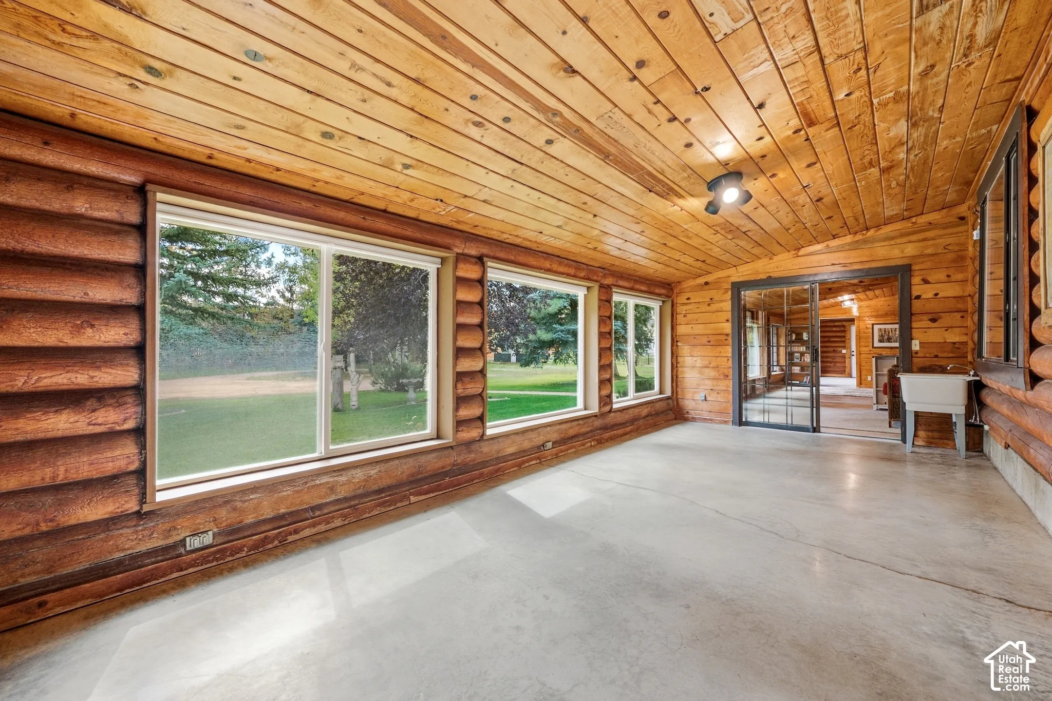 Spacious room featuring log construction, wood-plank ceilings, expansive windows, concrete flooring, and a ceiling-mounted light fixture