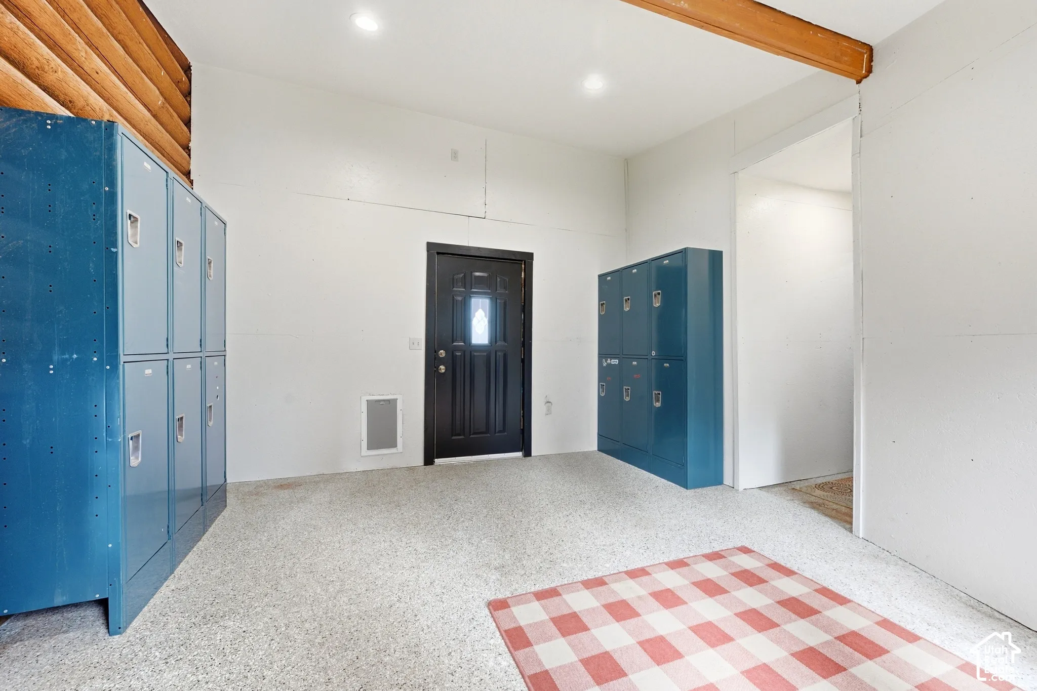 Recessed lighting, wood-finish ceiling beam, white walls, dark entry door with decorative glass, and light-colored speckled flooring