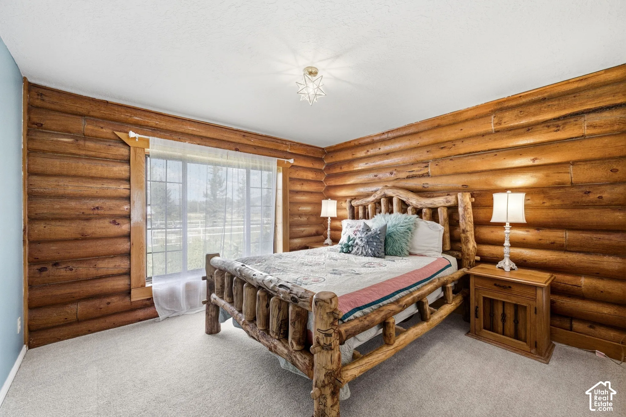 Log-style accent walls with exposed wood beams, window with exterior scenery, overhead light fixture, and light-toned carpeting