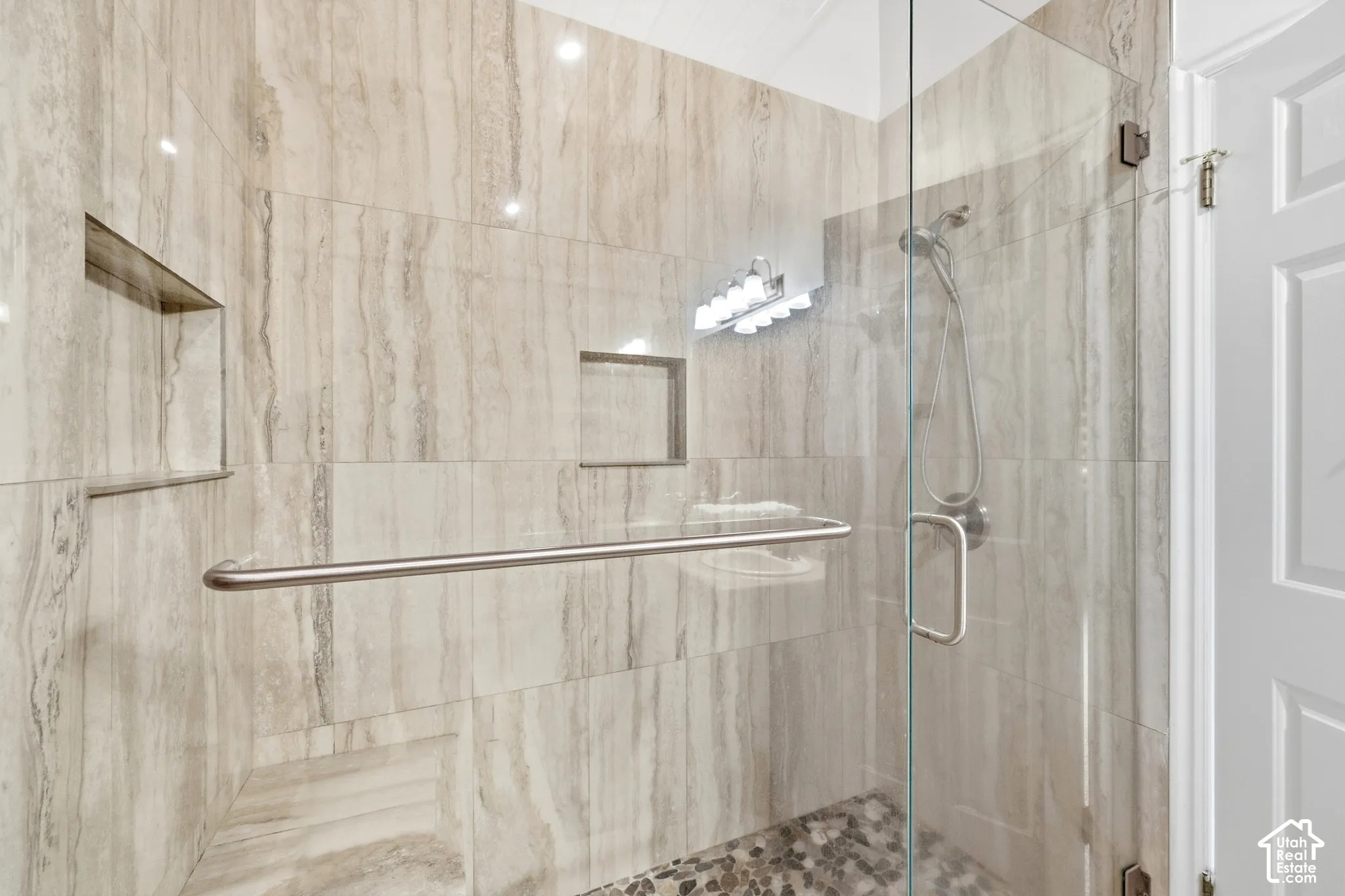 Glass-enclosed shower featuring natural stone-look wall tiling, recessed shelving, a built-in bench, and a pebble stone floor