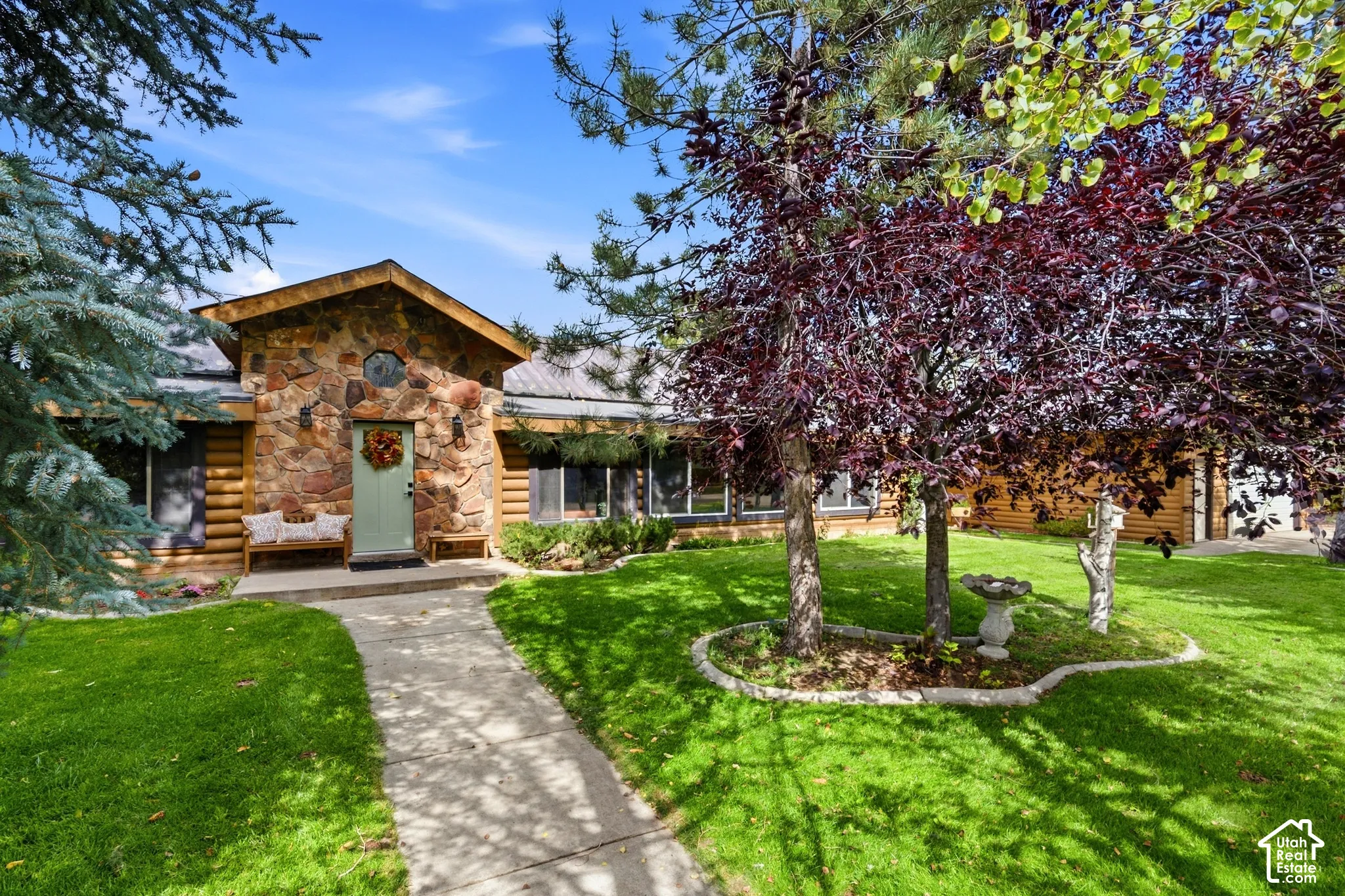 Stone facade entry with a light green door, log siding, gabled roofline, and a concrete pathway