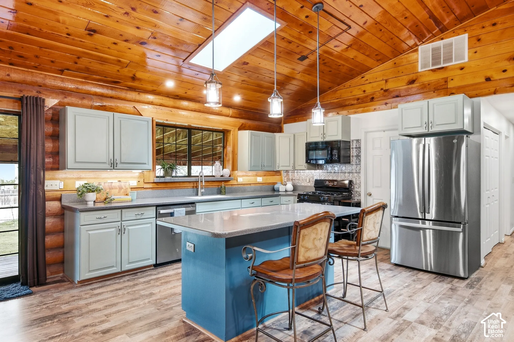 Vaulted wood-paneled ceiling with skylight, wood-finish flooring, light-toned cabinetry, stainless steel appliances, and a central island with countertop seating