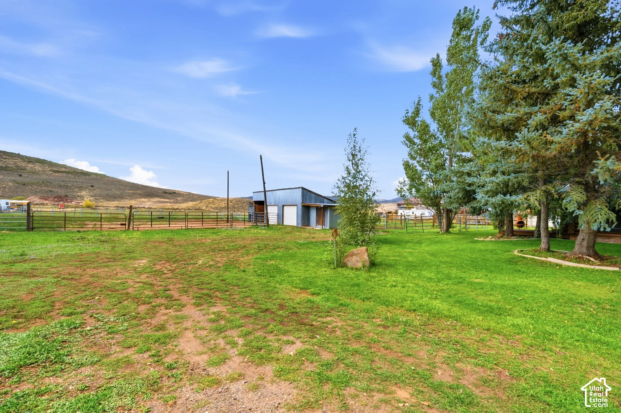 Expansive grassy area with mature trees, fenced enclosures, and a utility structure
