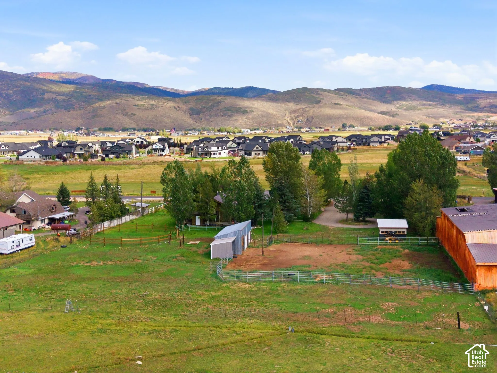 Expansive property featuring a large barn, multiple outbuildings, fenced enclosures, and mature trees, all set against a backdrop of distant mountains