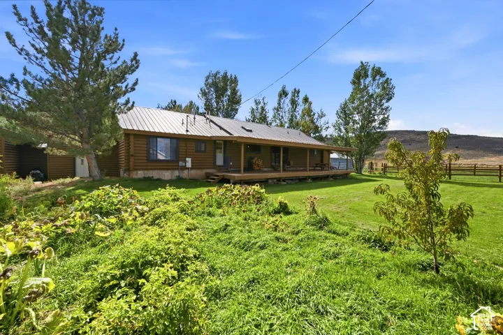 Log-sided residence with a metal roof, an expansive wooden porch, and an attached shed, set against a distant hillside