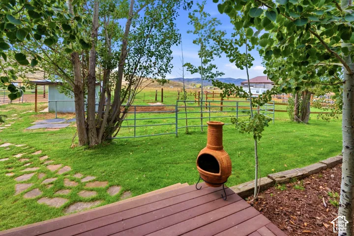 Expansive grassy yard with mature trees, a stone pathway, and a wood deck
