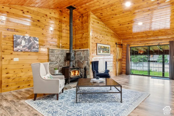 Vaulted wood-paneled ceiling, wood-paneled walls, stone-clad wood-burning stove, wood-finish flooring, and a sliding glass door