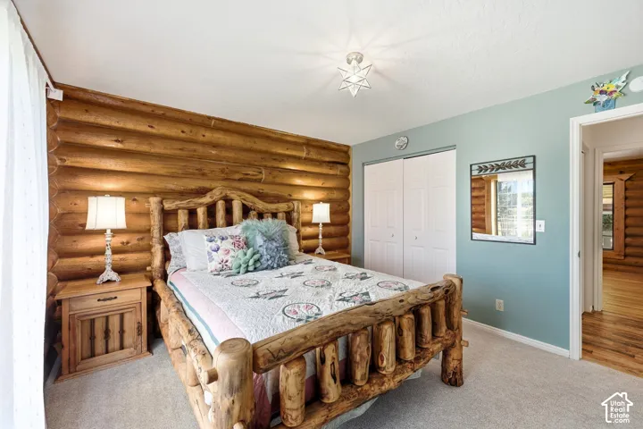Log wall accents, neutral carpet flooring, double closet doors, ceiling-mounted light fixture, and an interior doorway leading to wood-finish flooring