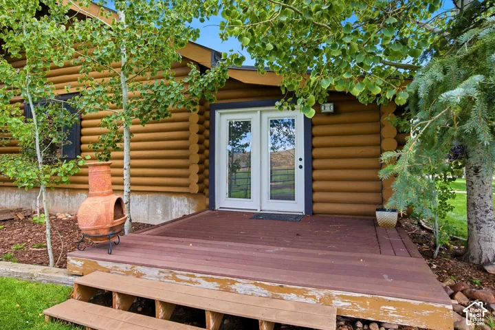 Log cabin exterior with a wood deck, white French patio doors, and natural landscaping