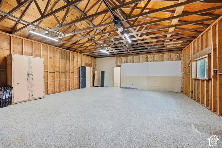 Exposed ceiling trusses, multiple flush-mount light fixtures, concrete flooring, and a single window