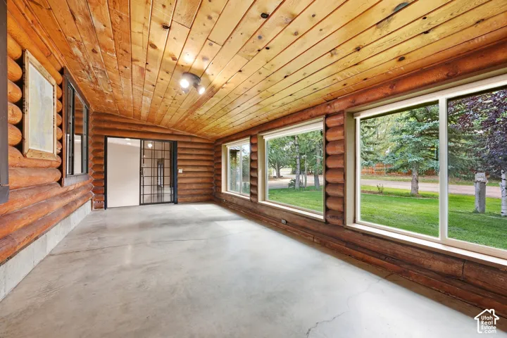 Log cabin-style enclosed porch with wood-paneled ceiling and walls, concrete flooring, and multiple large windows