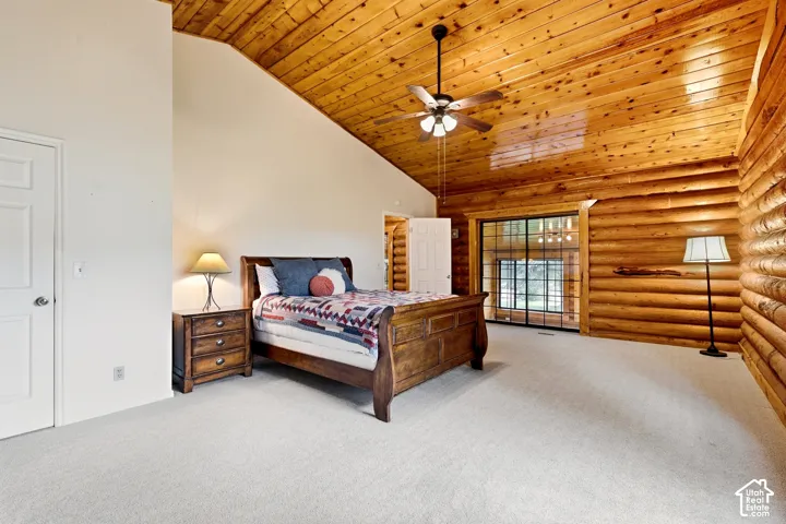 Vaulted wood-paneled ceiling with a ceiling fan, log walls, and light-colored carpeting