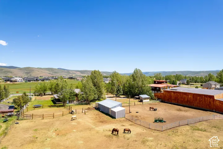 Expansive property with multiple fenced pasture areas, an enclosed barn structure, a large outbuilding, and distant mountain scenery