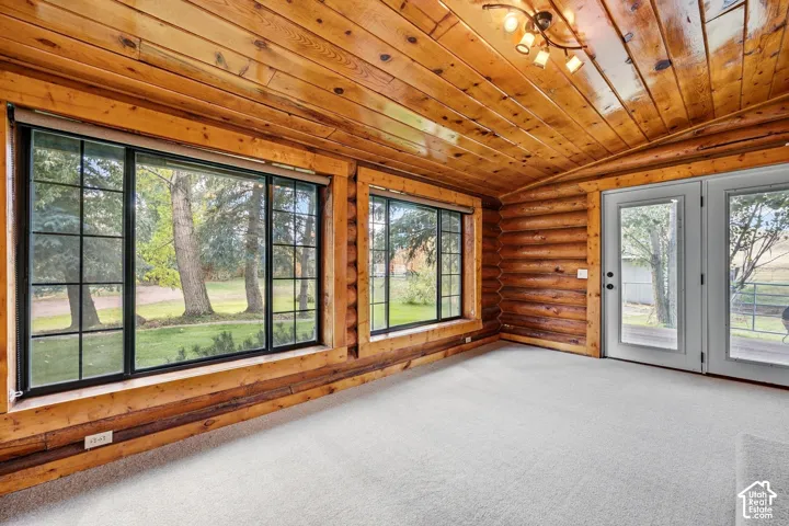 Wood-paneled ceilings, wood-log walls, light-toned carpeting, black-framed windows, and white-framed glass doors