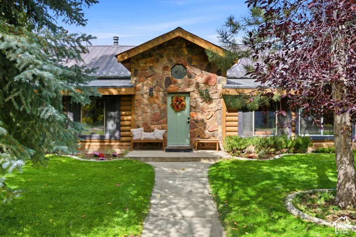 Stone and log exterior with a prominent entrance, metal roof, and established landscaping