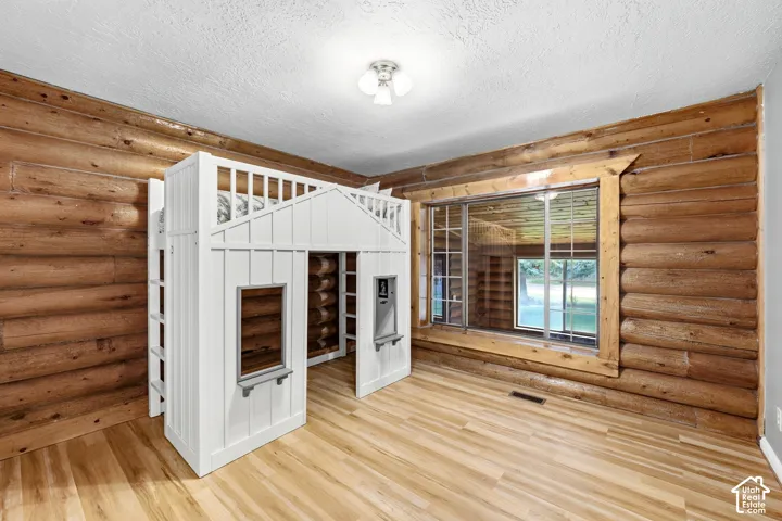 Log wall construction, wood-finish flooring, built-in loft bed with integrated playhouse, and a multi-pane window