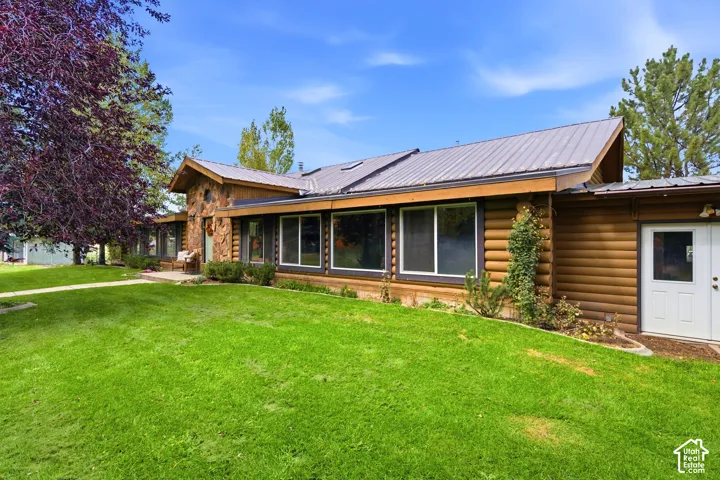 Log cabin exterior with stone accents, a gray metal roof, multiple large windows, and a manicured lawn