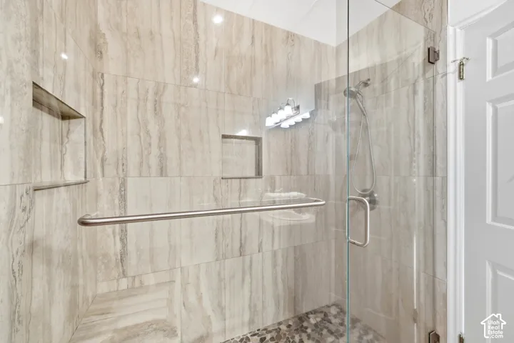 Glass-enclosed shower featuring natural stone-look wall tiling, recessed shelving, a built-in bench, and a pebble stone floor