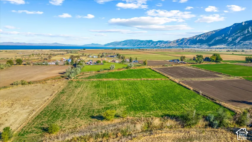 Expansive land featuring cultivated fields, distant mountain ranges, and a large body of water