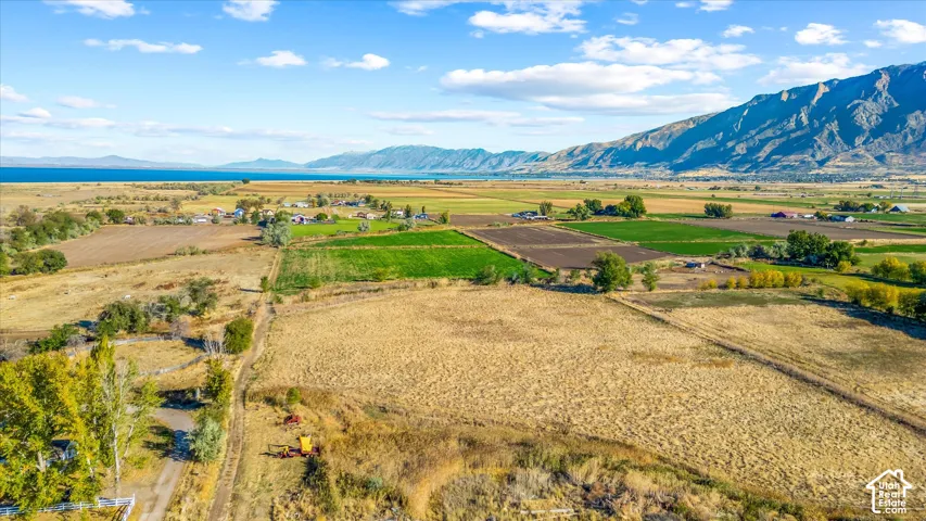 Expansive land with varied terrain, including cultivated fields and natural growth, set against a backdrop of mountains and a large body of water