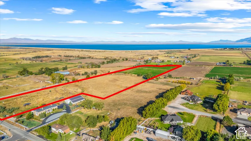 Expansive land parcel featuring open fields, distant water body, and surrounding rural properties