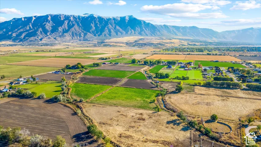 Expansive agricultural land featuring a mountainous backdrop, varied field cultivation, and scattered residential properties