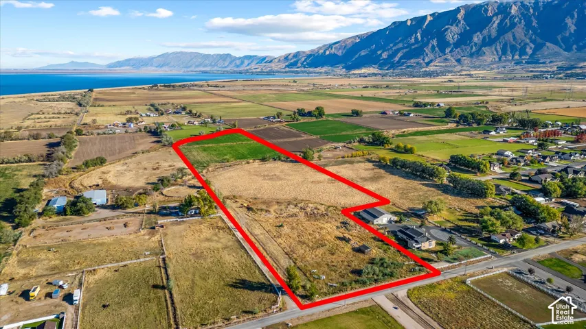 Expansive agricultural land with clear boundaries, bordered by a paved road, mountains, and a body of water