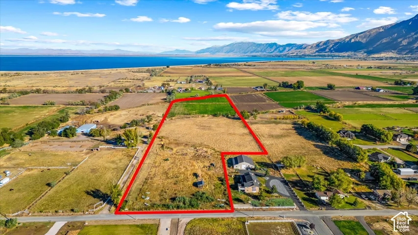 Expansive land parcel featuring open fields, distant water body, and mountain backdrop