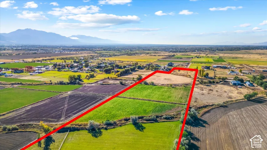 Expansive open land with varied agricultural fields, surrounded by established trees and distant mountain ranges