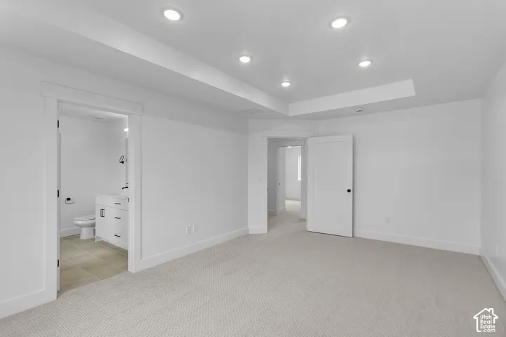 Recessed ceiling lights, tray ceiling detail, white paneled doors, light-toned carpeting, and a full bathroom with vanity