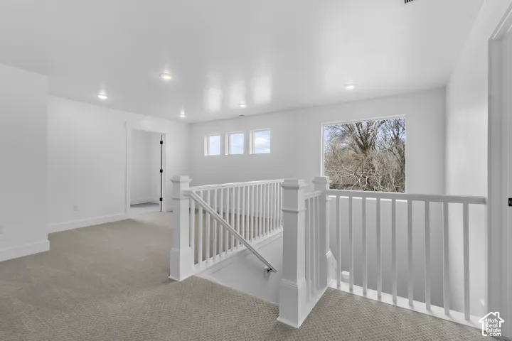 Carpeted loft area with recessed lighting, white baluster railing, and multiple windows