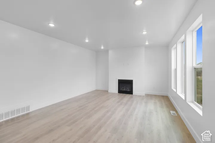 Recessed ceiling lighting, light wood-finish flooring, built-in fireplace, multiple windows, and white walls