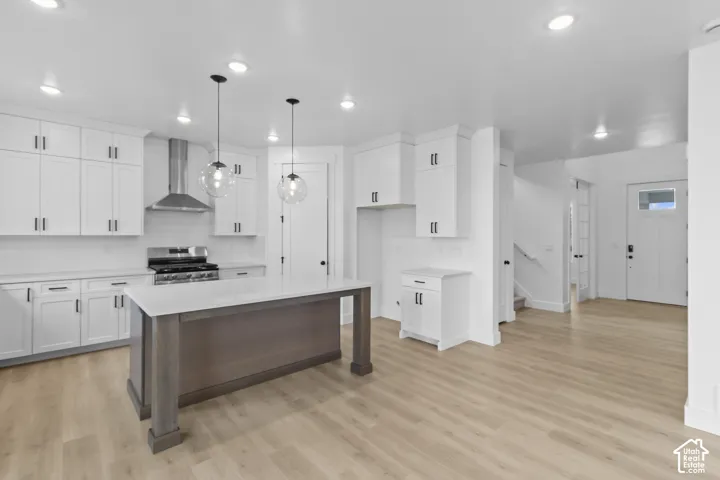 White shaker-style cabinetry, stainless steel range with hood, wood-finish flooring, island with contrasting base, and recessed lighting