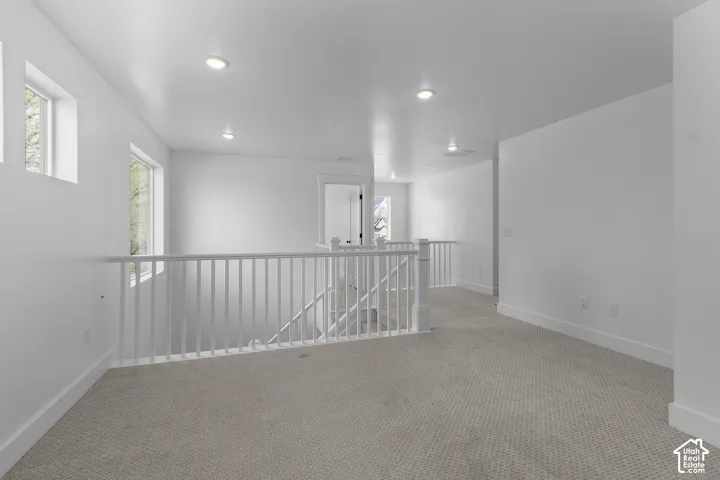 Carpeted landing featuring white railings, multiple windows, and recessed lighting