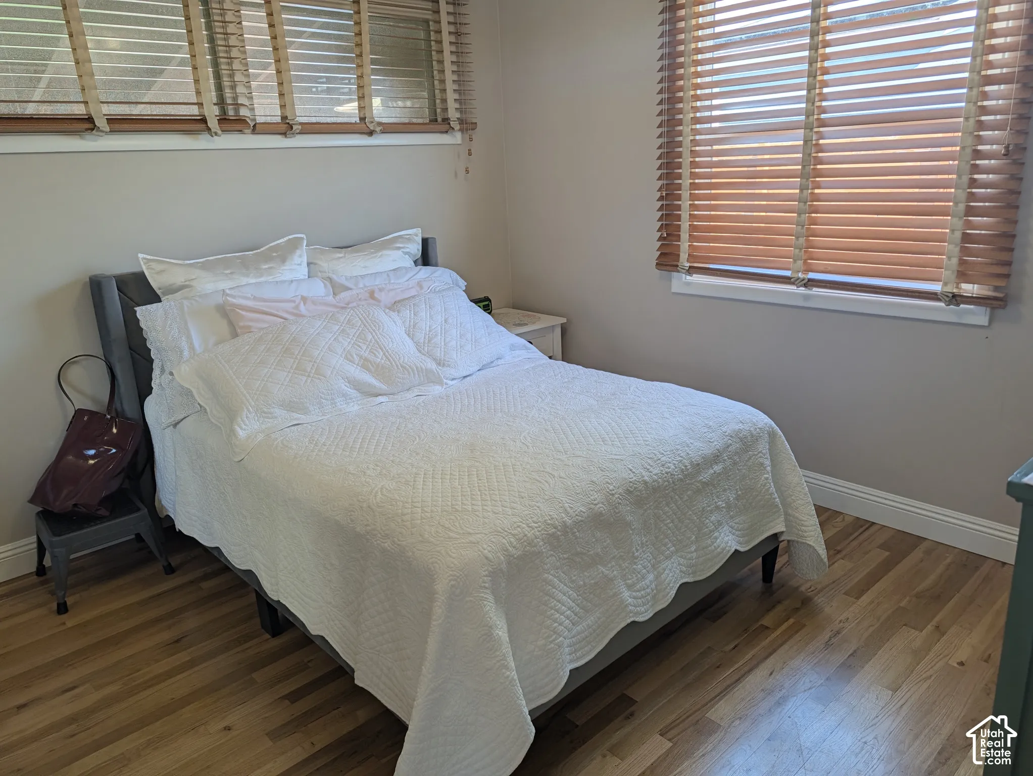 Warm wood-finish flooring with light wall tones and multiple windows featuring wood blinds