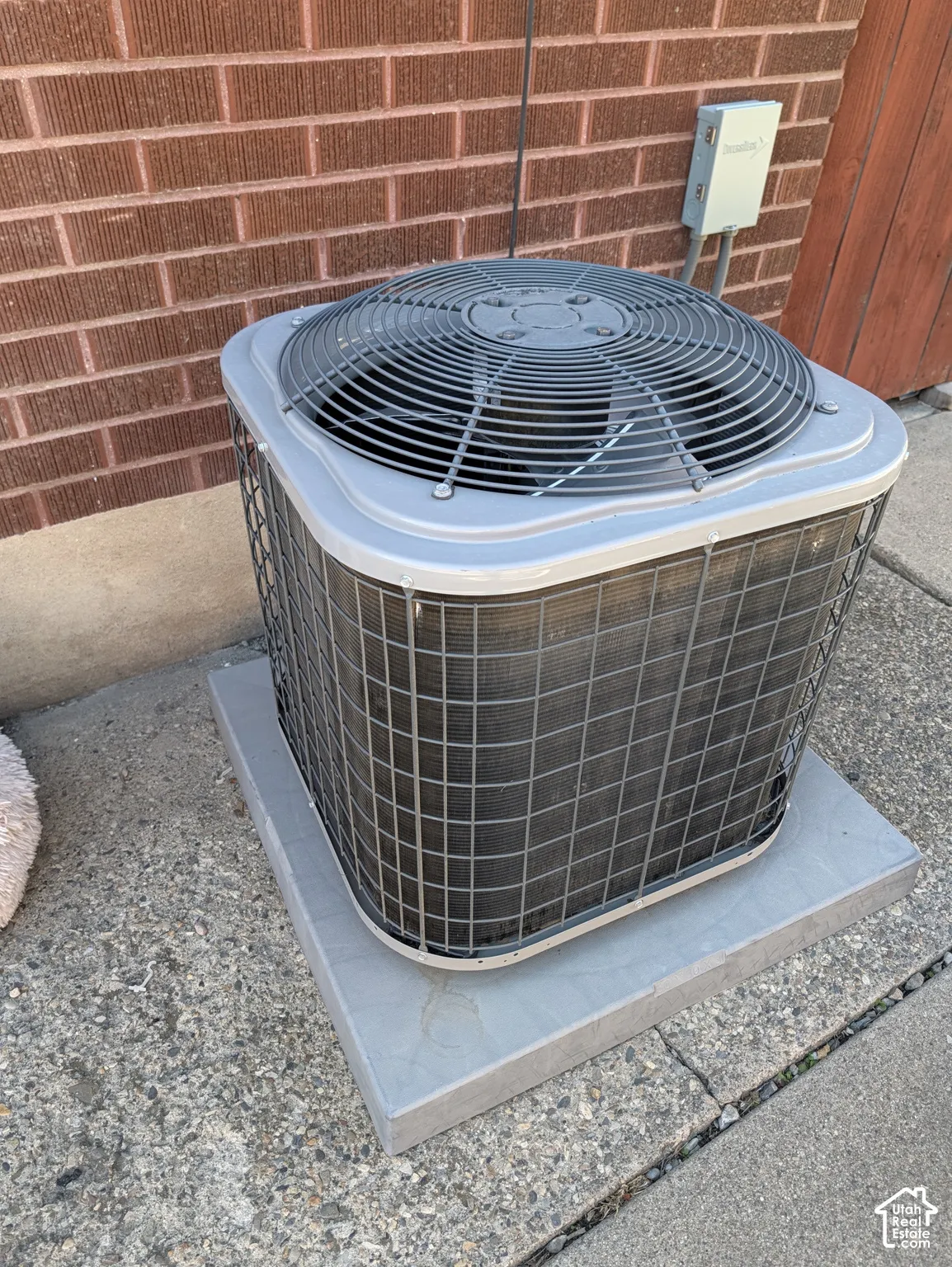 Exterior HVAC unit on a concrete pad with a brick wall backdrop