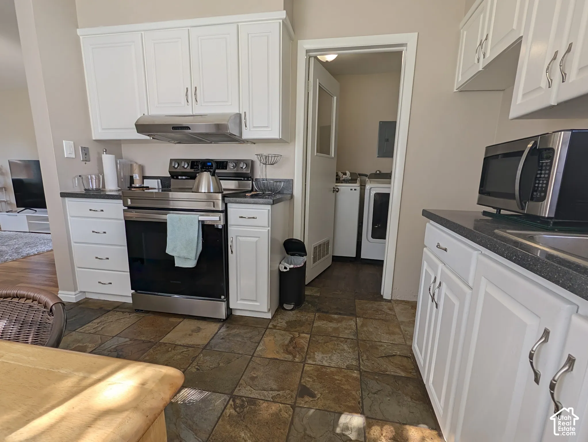 White cabinetry with brushed nickel hardware, stainless steel appliances, dark stone countertops, and multi-toned tile flooring