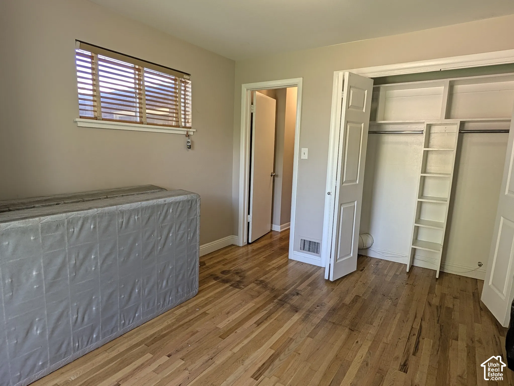 Hardwood flooring, neutral wall tones, window with wood-finish blinds, bi-fold closet doors, and built-in closet shelving