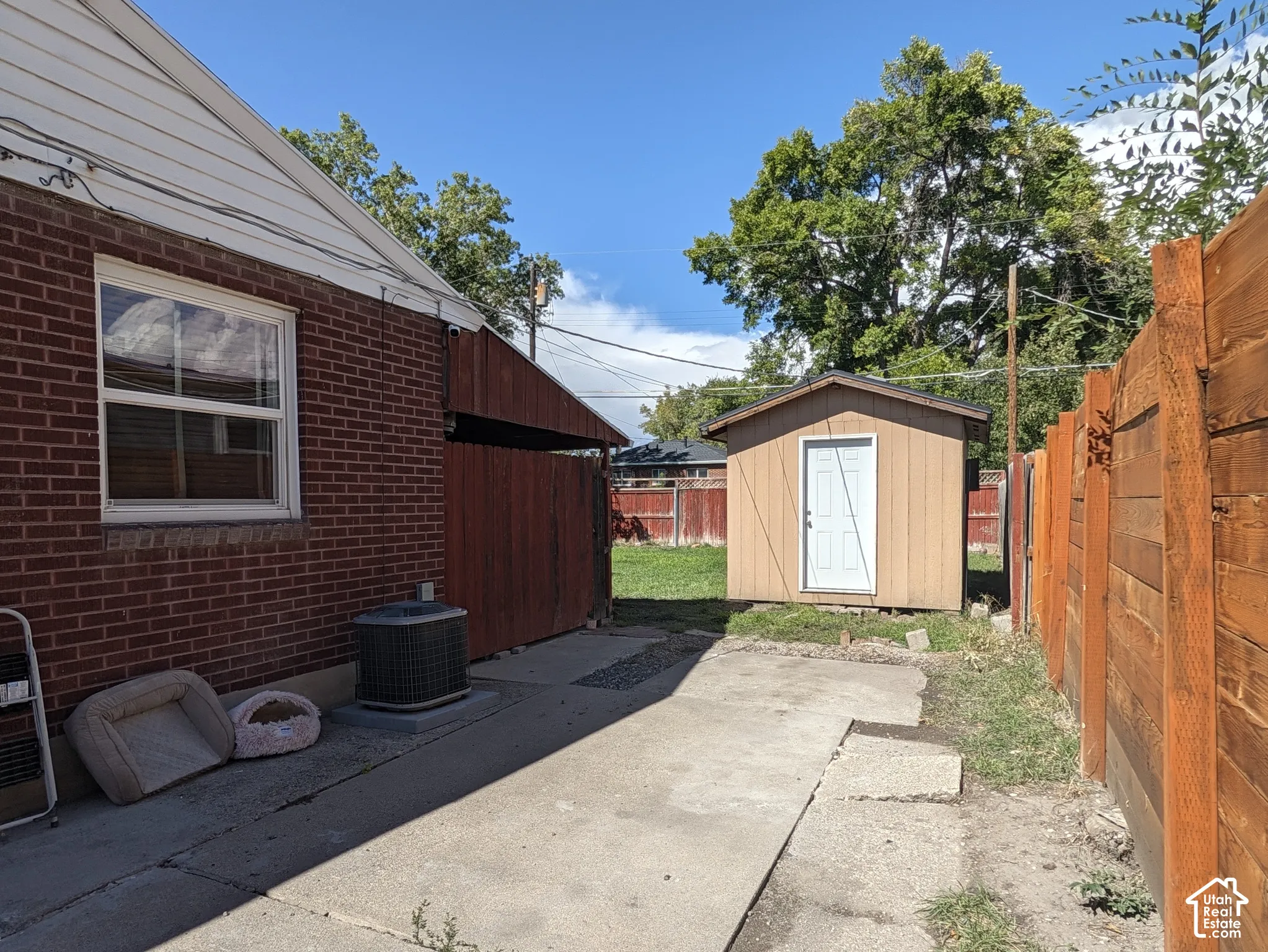 Brick exterior with white window trim, wood privacy fencing, concrete walkway, and a detached storage shed