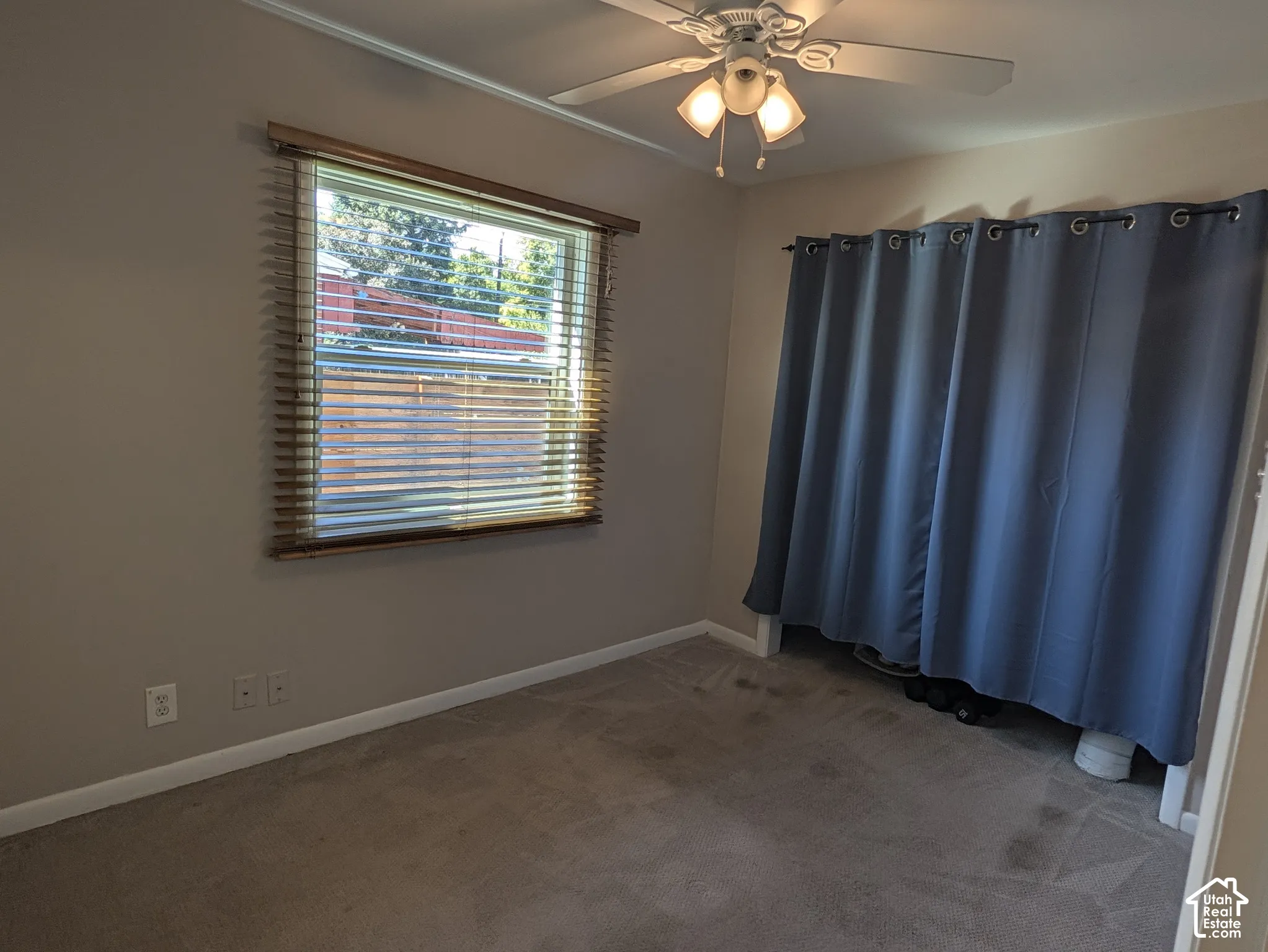 Carpeted room featuring a window with horizontal blinds and a ceiling fan with light fixture