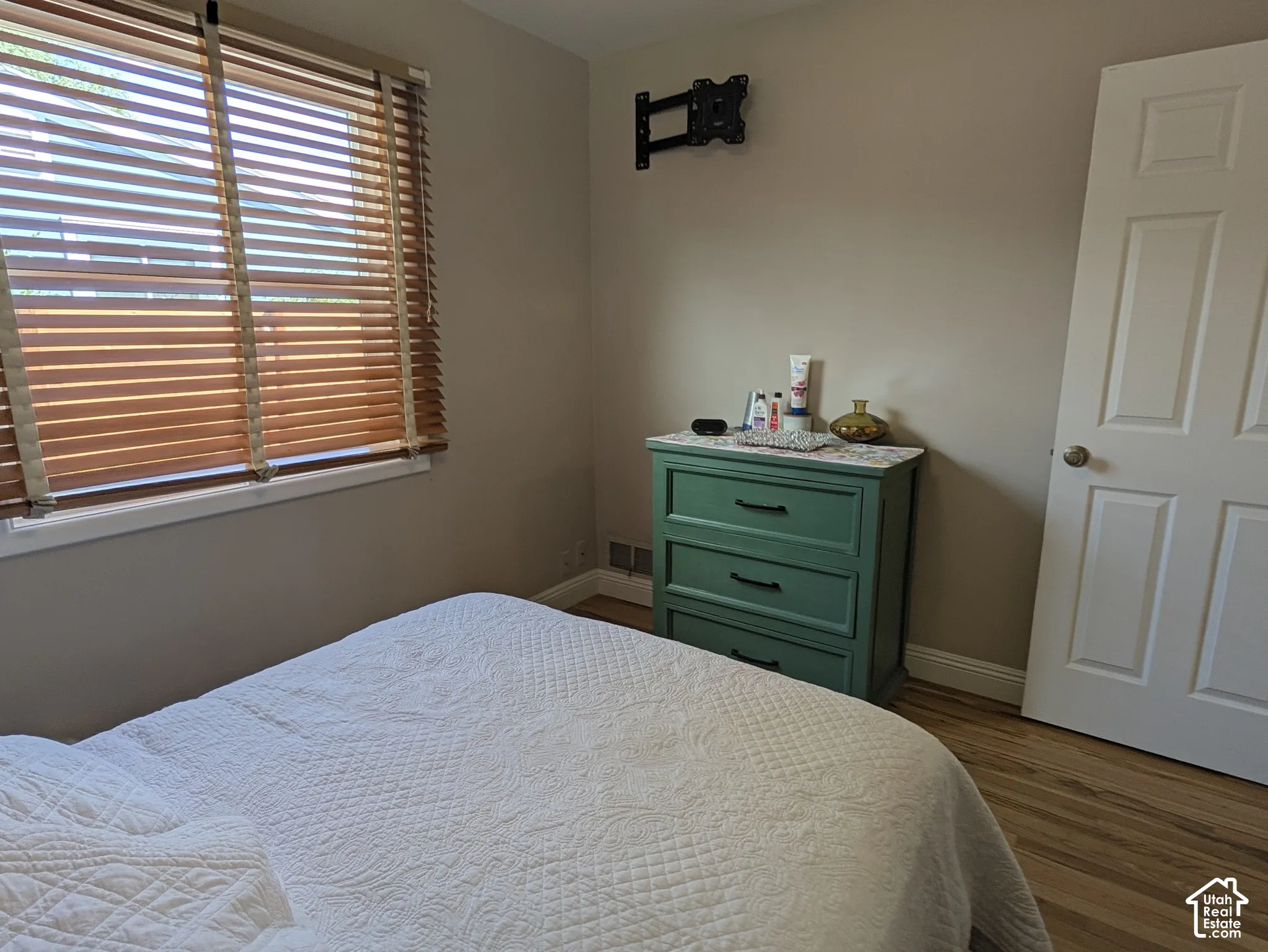 Window with horizontal blinds, neutral wall paint, wood-finish flooring, white paneled door, and white trim