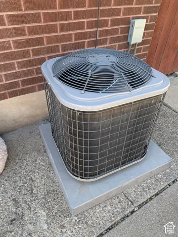 Exterior HVAC unit on a concrete pad with a brick wall backdrop