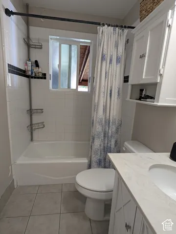 White tile bath surround with a black accent band, white bathtub, frosted window, white vanity with an integrated sink, and light-toned tile flooring