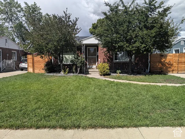Brick exterior featuring mature trees, a manicured lawn, and a light wood-finish privacy fence