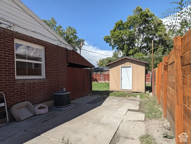 Brick exterior with white window trim, wood privacy fencing, concrete walkway, and a detached storage shed